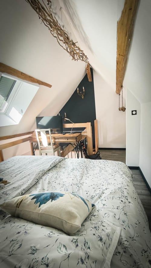 Chambre mansardée cosy au Clos du Buisson : lit double, literie fleurie, poutres apparentes, bureau et vue sur le jardin