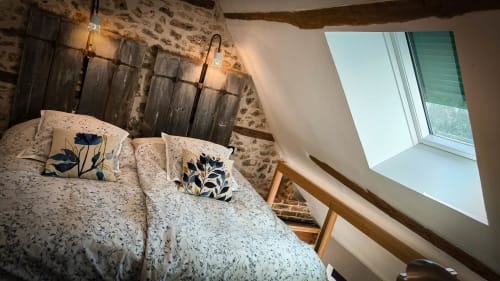 Chambre double cosy au Clos du Buisson avec murs en pierre, oreillers à fleurs, puits de lumière et vue sur le jardin
