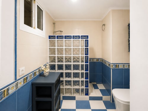 Moderno baño con piso de cuadros azules y blancos, mampara de ducha de bloques de vidrio y bordes decorativos de azulejos en Holibai
