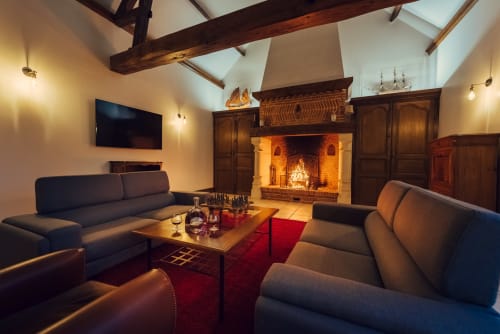 Salon luxueux au Clos Céleste avec foyer, poutres apparentes, canapés en cuir et ambiance chaleureuse à Ecrainville.