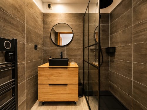 Salle de bain moderne avec meuble vasque en bois, lavabo noir, miroir rond et douche à l'italienne à L'Île-Rousse