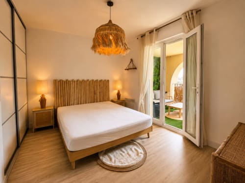 Chambre moderne de l'appartement L'Île-Rousse avec lit en bois, luminaires suspendus et accès à terrasse vue montagne