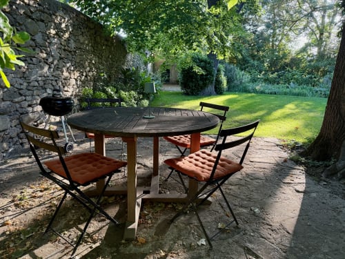 Table de salle à manger ronde en extérieur avec chaises et coussins rouges sur la terrasse du gîte Domaine de Montlaur en Val-de-Dagne, France