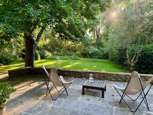 Terrasse en pierre ombragée avec fauteuils papillon et table au gîte Domaine de Montlaur à Val-de-Dagne, avec vue sur jardin