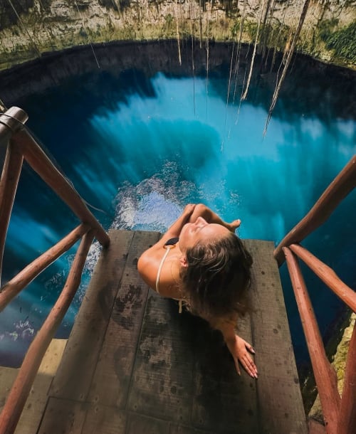 Huésped relajándose en plataforma de madera sobre cenote turquesa en Hotel Boutique Cenote Secreto Maya, Valladolid Yucatán