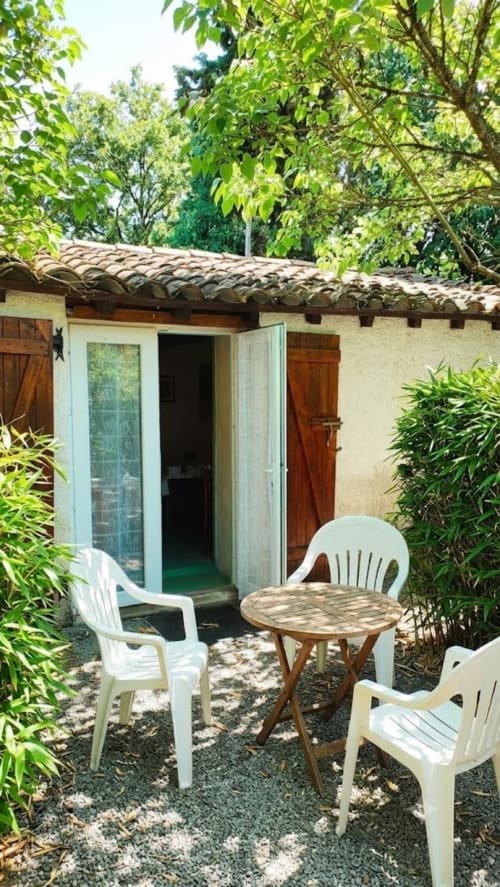 Garden view patio at Le Portel des Arnaud with white chairs, wooden table, and lush green surroundings in French countryside