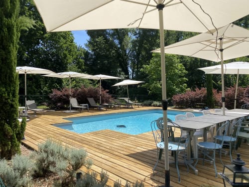 Baccara Lodge pool area with wooden deck, blue swimming pool, dining tables under umbrellas, and green landscaping in
