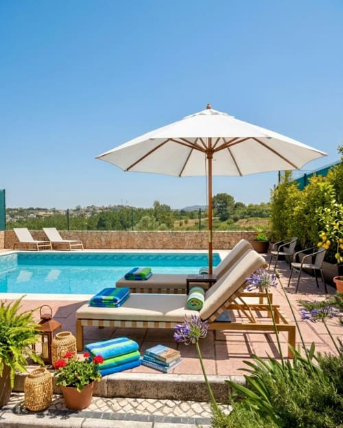 Luxury villa pool area in Sesimbra with lounger, umbrella, blue water, and scenic garden views