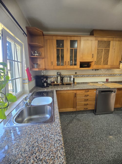 Modern kitchen with wooden cabinets, granite countertops, stainless steel appliances, and window overlooking garden at Casa