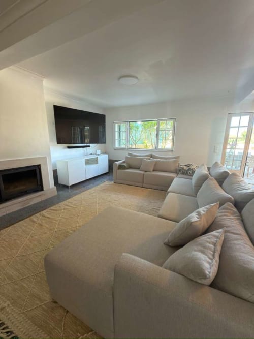 Modern living room with beige sectional sofa, fireplace, flat-screen TV, white entertainment unit, large windows with garden