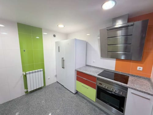 Modern kitchen in Casa Forever Young villa with green cabinets, stainless steel appliances, and orange tile accents,