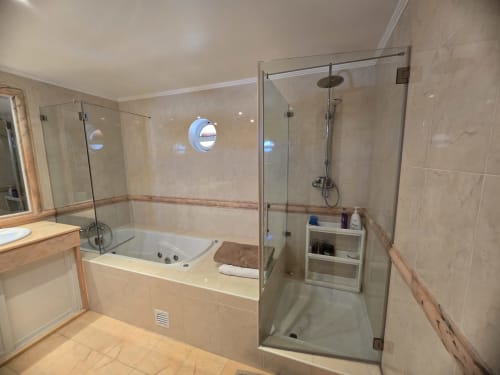 Modern bathroom in Casa Forever Young villa with glass shower enclosure, soaking tub, and beige tile finishes
