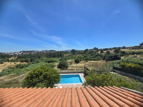 Aerial view of Casa Forever Young villa in Sesimbra with private blue swimming pool, terracotta roof, and rolling countryside