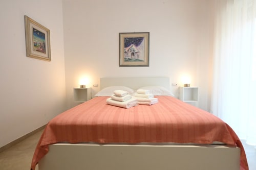 Chambre d'hôtel moderne au Melo 48 Bari avec couvre-lit corail, tête de lit blanche, lampes de chevet et tableaux encadrés sur murs beiges