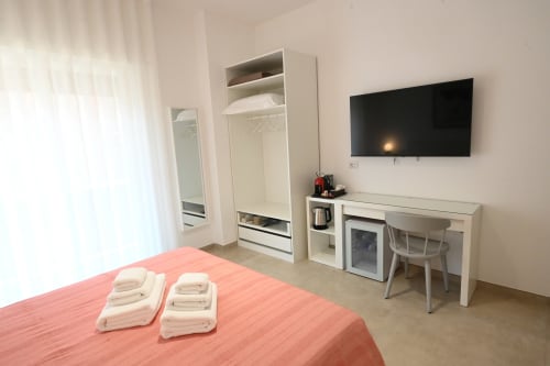 Chambre d'hôtel moderne au Melo 48 à Bari avec couverture corail, TV écran plat, bureau, armoire et vue sur la ville