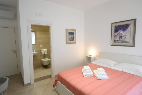 Chambre lumineuse à l'hôtel Melo 48 à Bari avec lit double, salle de bain attenante, télévision écran plat et tableaux encadrés