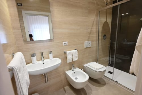 Salle de bains moderne de l'hôtel Melo 48 à Bari avec double vasque, bidet, toilettes, douche à l'italienne et radiateur sèche-serviettes