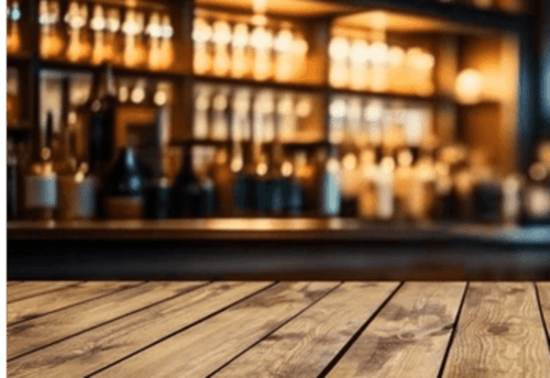 Wooden bar counter with blurred bottles and warm lighting at Clos Céleste boutique hotel in Ecrainville, France