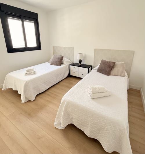 Dormitorio doble con colchas acolchadas blancas, cabeceros beige y suelos de madera en cabaña de Benalmádena