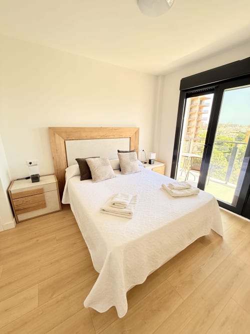 Dormitorio moderno con cama de marco de madera, ropa de cama blanca y vistas a la ciudad desde el balcón en la cabaña Sinese Design Homes