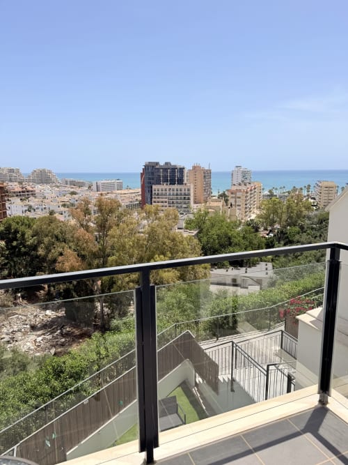 Vista del balcón de la costa de Benalmádena con el mar Mediterráneo, edificios frente a playa y vegetación exuberante desde casa familiar