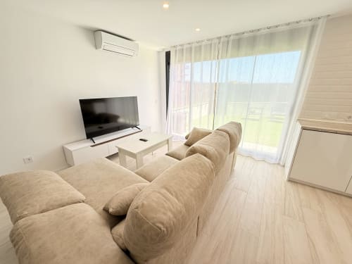 Luminosa sala de estar con sofá beige, televisor y puertas de cristal con vistas a Benalmádena en cabaña moderna