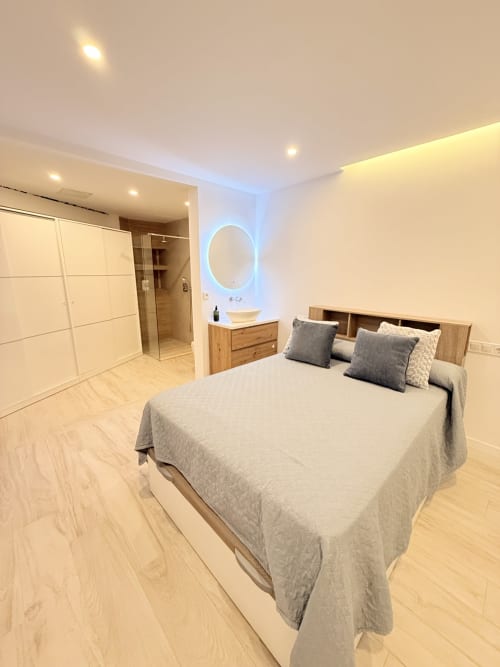 Dormitorio moderno con baño en suite en casa rural de Benalmádena, con cama de matrimonio, cabecero de madera, espejo iluminado y