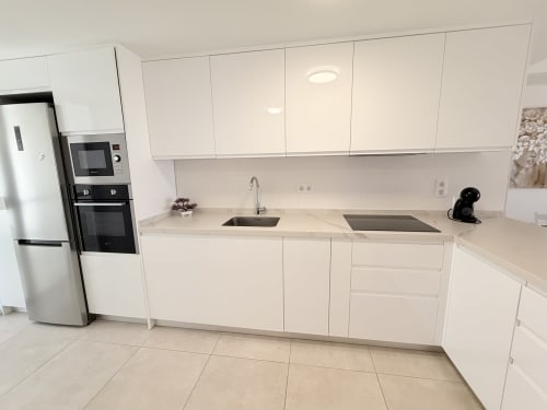 Cocina moderna blanca con electrodomésticos de acero inoxidable, encimera de granito y fregadero en casa rural de Benalmádena