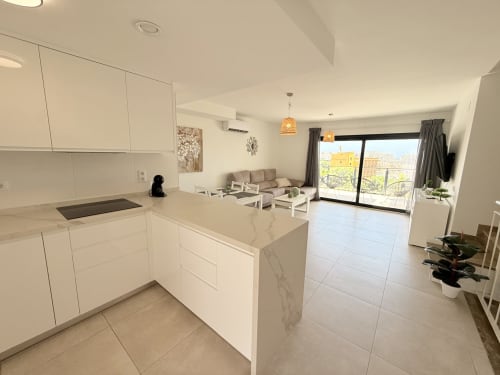 Cocina y sala de estar de planta abierta en Benalmádena con muebles blancos, isla de mármol y vistas a la terraza