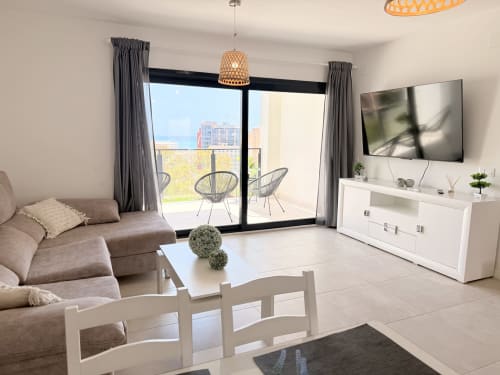 Sala de estar moderna con sofá beige, televisor y amplio balcón con vistas a la ciudad de Benalmádena en casa familiar