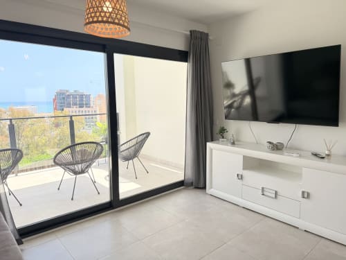 Salón moderno en casa de Benalmádena con TV de pantalla plana, muebles blancos y balcón con vistas al mar