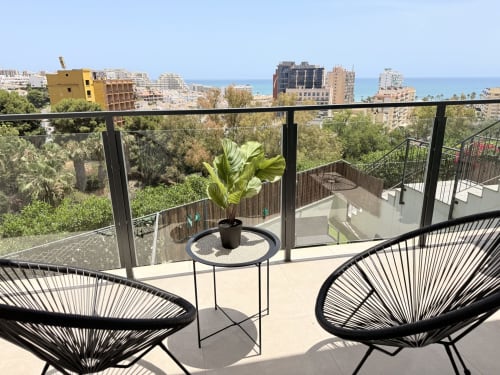 Terraza costera con sillas de huevo negro con vistas a Benalmádena, el mar Mediterráneo y edificios frente al mar con plantas en macetas
