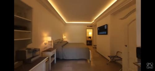 Modern bedroom in Villa D'Alessandro apartment with ambient ceiling lighting, bed, desk, TV, and warm contemporary design in