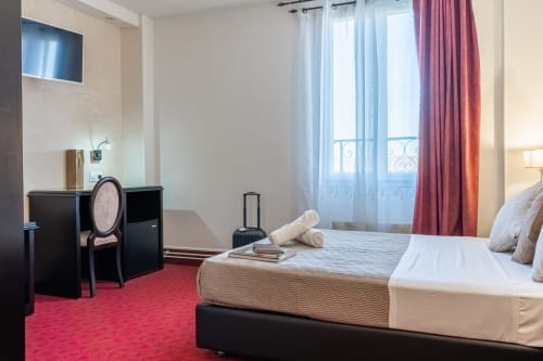 Chambre Hotel Royal Paris Ivry avec lit queen-size, bureau, moquette rouge et portes-fenêtres style parisien