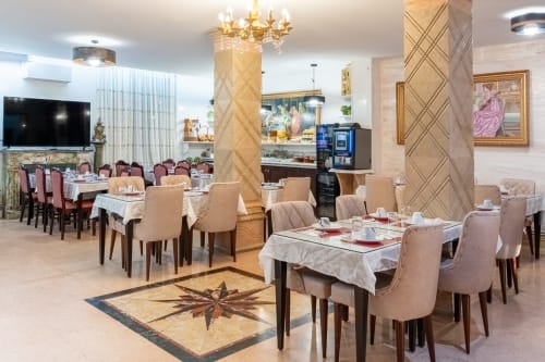 Élégante salle à manger de l'Hôtel Royal Paris Ivry avec chaises beiges, nappes blanches, colonnes décoratives et cristal