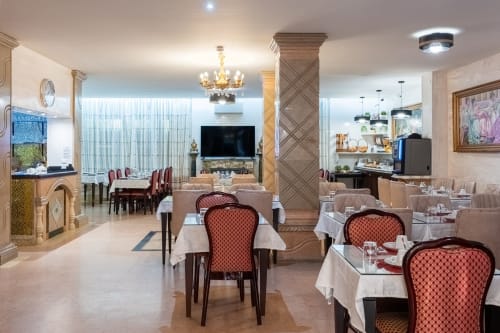 Salle à manger élégante de l'Hôtel Royal Paris Ivry avec chaises rouges à motifs, nappes blanches et lustre orné