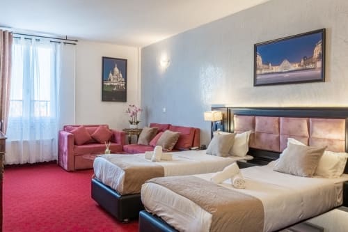 Habitación doble del Hotel Royal Paris Ivry con camas gemelas, sofá rosa y obras de arte de monumentos parisinos