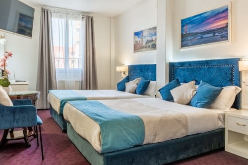 Suite Deluxe bedroom at Hotel Royal Paris Ivry featuring twin beds with blue velvet headboards and city view windows