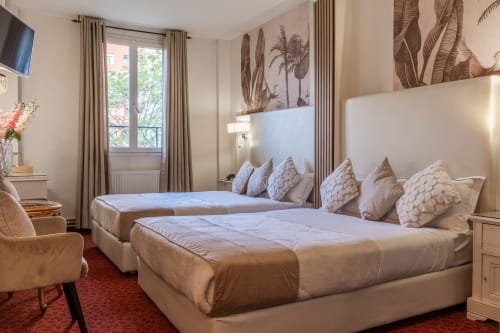 Deluxe Suite at Hotel Royal Paris Ivry featuring two beds with decorative pillows, tropical artwork, and elegant beige décor