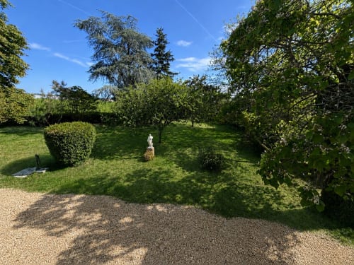 Les jardins luxuriants du Château Alto Cormeil à Saint-Émilion avec haies taillées, arbres matures et allées gravillonnées.