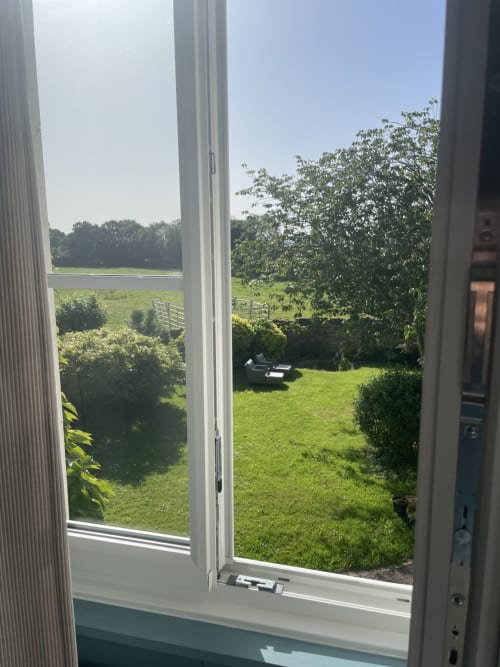 Vue du jardin depuis la Chambre Houlgate au domaine de Marculfo, avec pelouse verdoyante, haies et arbres à Saint-Marcouf