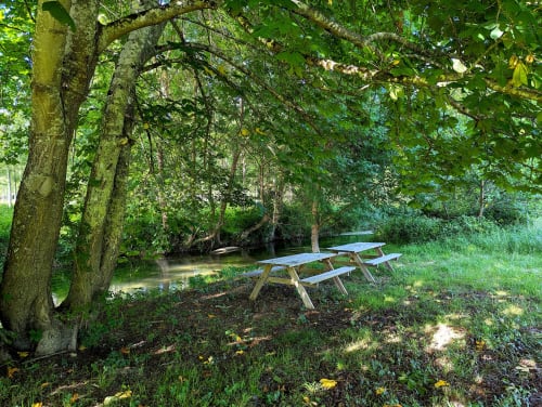 Tables de pique-nique en bois au bord d'un ruisseau paisible sous les arbres feuillus du Domaine Alga B&B, Bourg-Charente