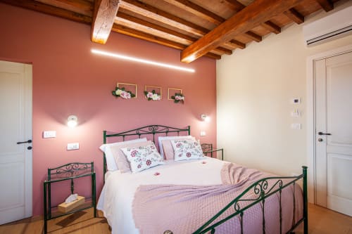Camera da letto in agriturismo a Pienza con pareti color corallo, travi in legno a vista, letto in ferro battuto e vista sul giardino