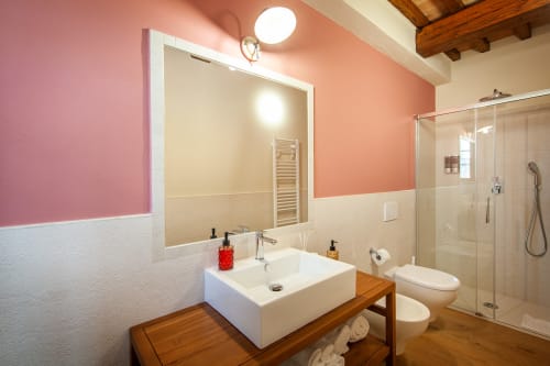 Bagno moderno all'Agriturismo Marinello di Pienza con pareti rosa corallo, lavabo bianco, mobile in legno e doccia in vetro