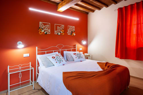 Camera luminosa dell'Agriturismo Marinello a Pienza con pareti rosse vivaci, letto in metallo bianco e quadri floreali