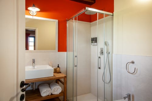 Bagno moderno presso l'Agriturismo Marinello a Pienza con parete accent arancione, lavabo a vessel, doccia in cristallo e dettagli in legno