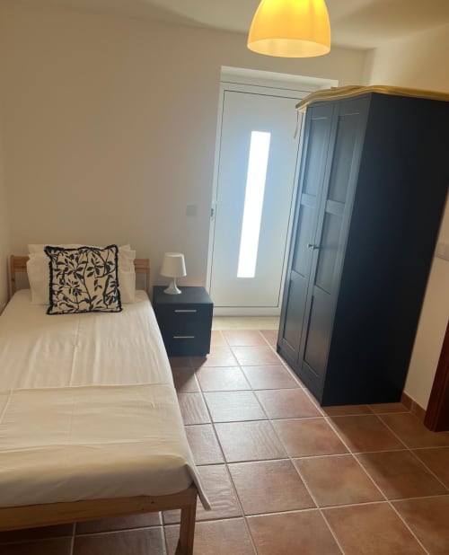 Bright bedroom with single bed, black wardrobe, and terracotta tiles in Casa Dourada villa, Aljezur, Portugal