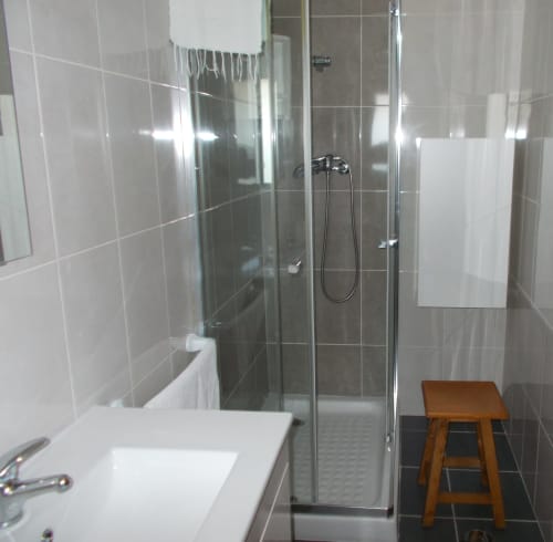 Modern bathroom with glass-enclosed shower, white sink, and wooden stool in Casa Dourada villa, Aljezur