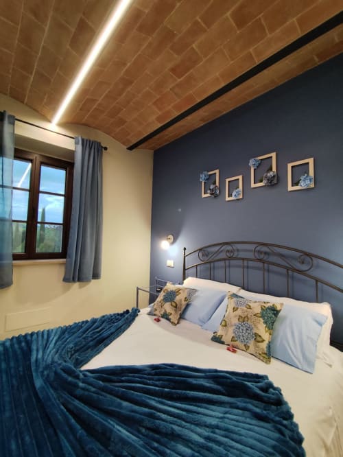 Modern bedroom at Agriturismo Marinello in Pienza with wrought iron bed, blue accents, dark feature wall, exposed brick
