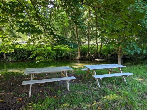 Tables de pique-nique au bord d'une rivière paisible au Domaine Alga B&B à Bourg-Charente, entourées d'arbres verdoyants